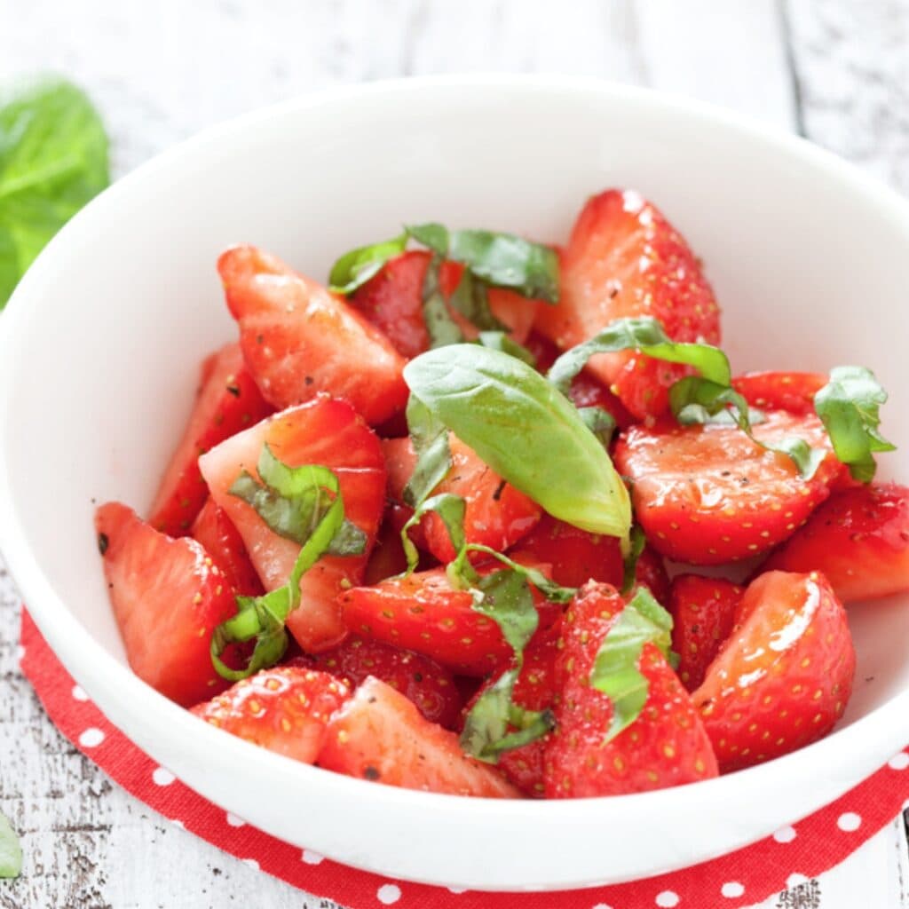 Bowl of Sliced Fresh Strawberries Drizzled with Oil and Seasoned with Black Pepper and Basil