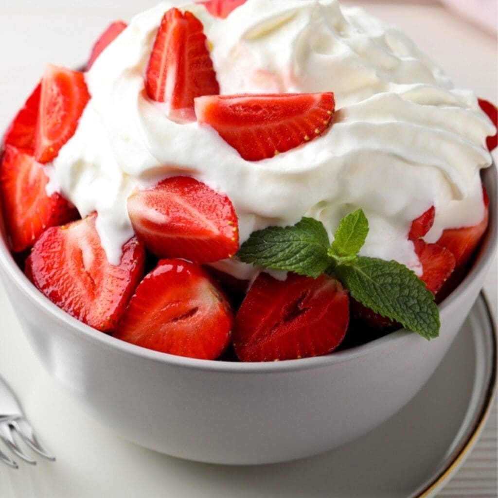 Bowl of Sliced Fresh Strawberries Topped With Whipped Cream and a Sprig of Mint