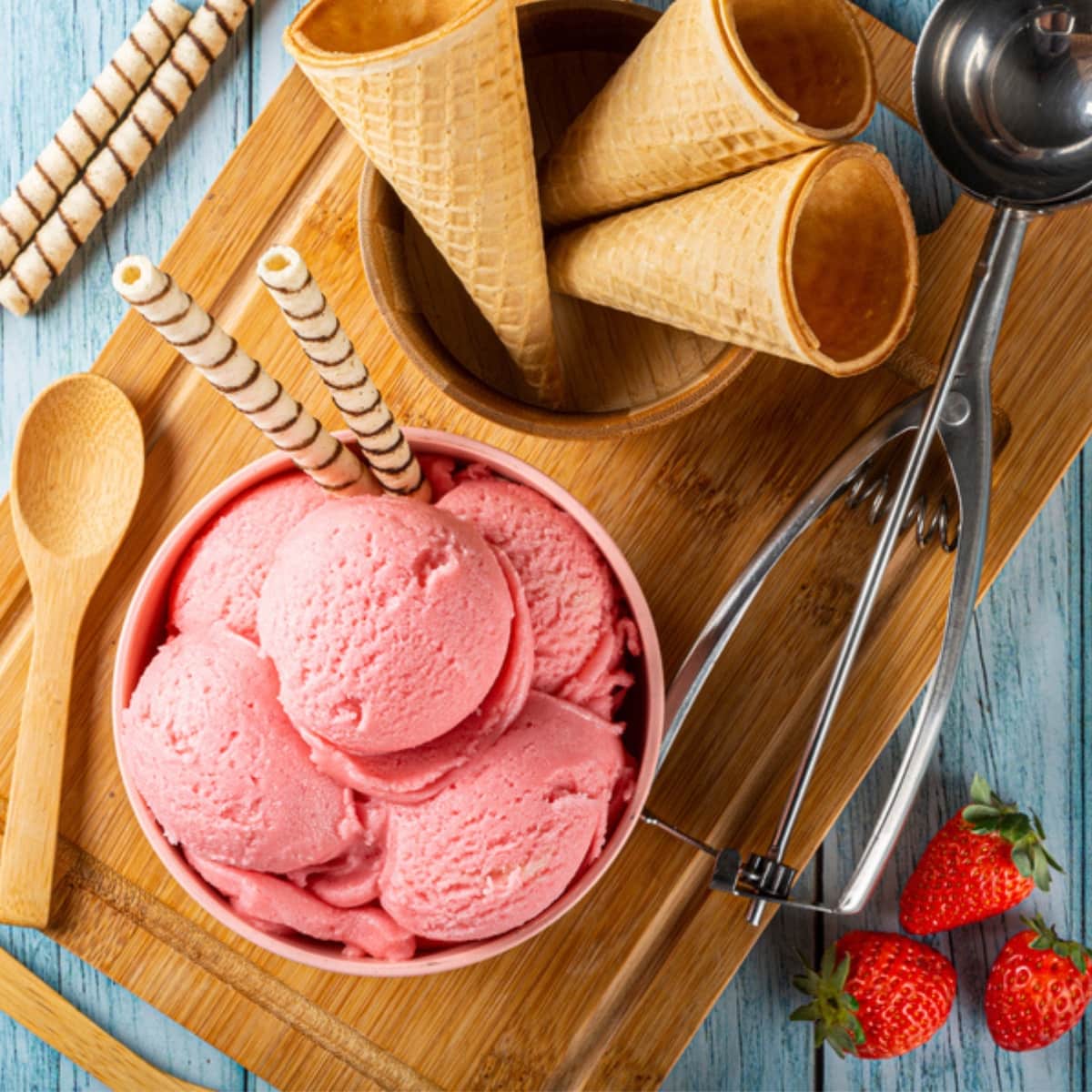 Strawberry ice cream, cones, and a wooden board.