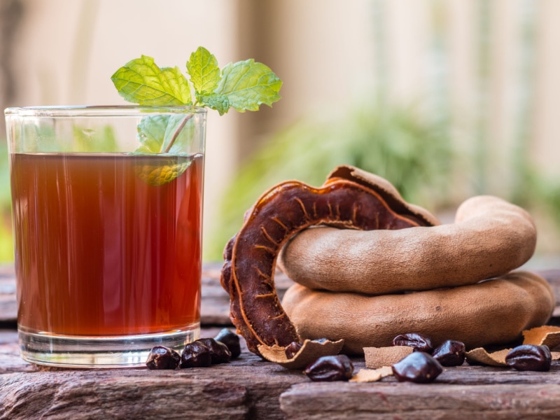 A Glass of Tamarind Juice and Ripe Tamarinds on a Wooden Table