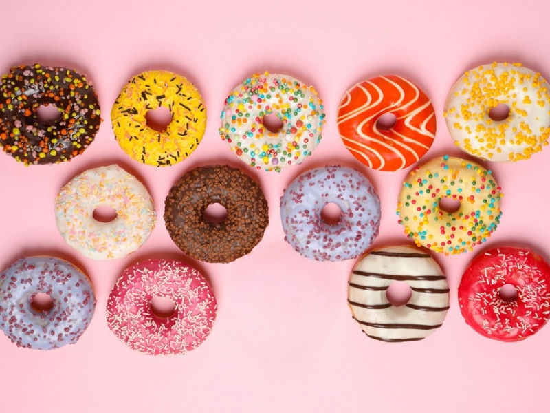 Thirteen Different Flavored and Colored Donuts on a Pink Background