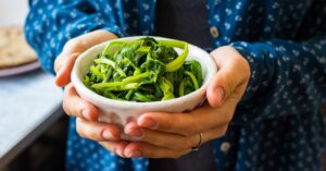 Woman Holding Cooked Steamed Spinach in a White Bowl