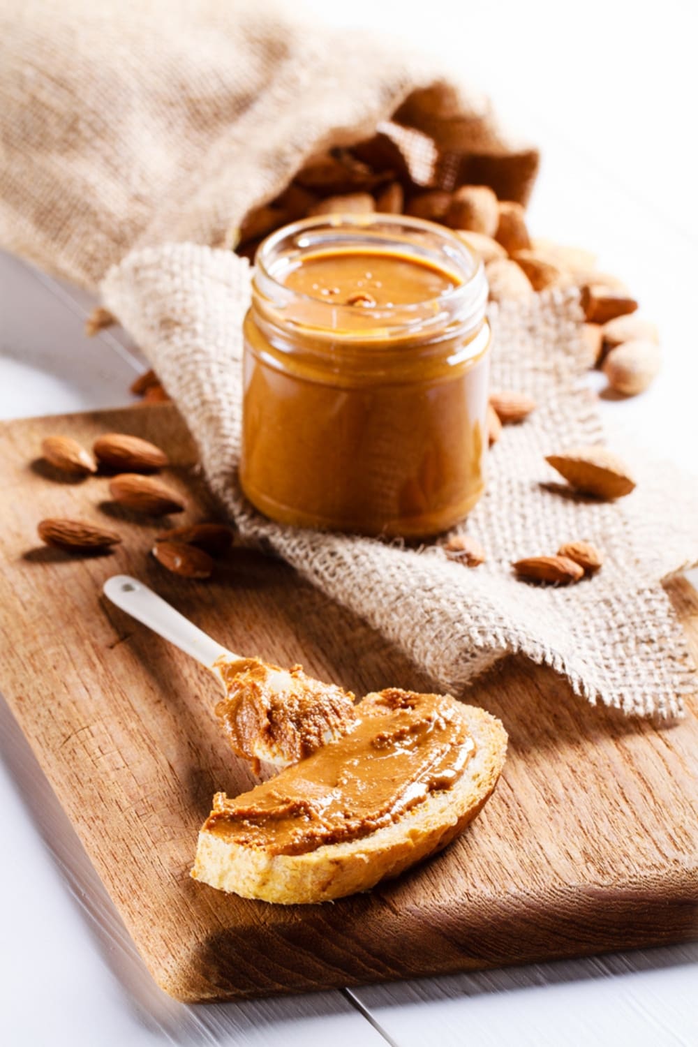 Jar of Homemade Almond Butter on a Burlap Sack with Slice of Bread With Almond Butter in Foreground