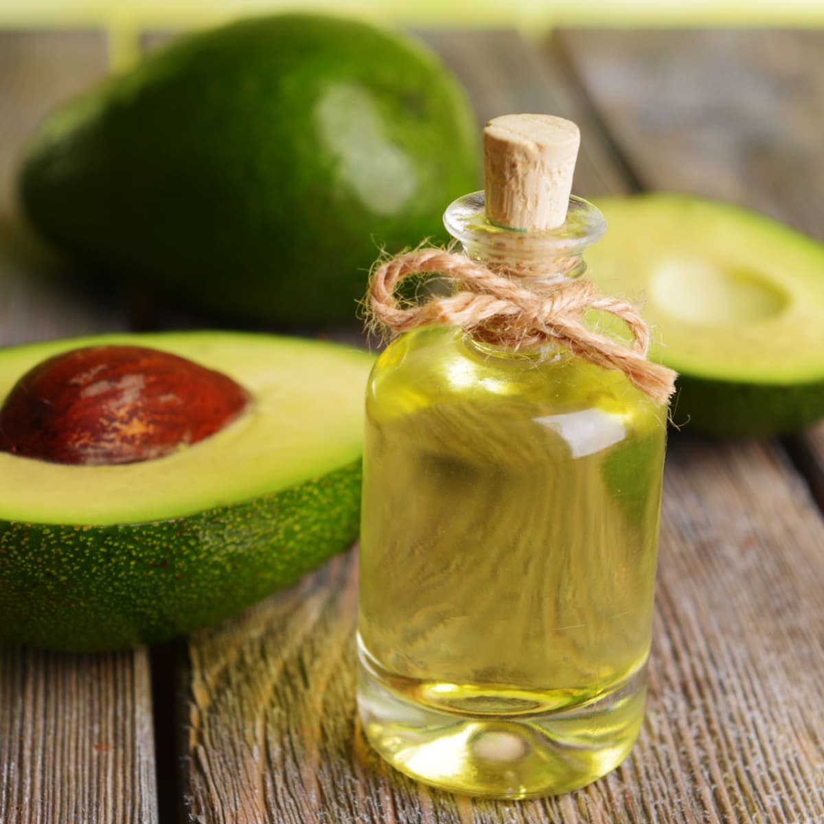 A Bottle of Avocado Oil and Fresh Avocados on a Wooden Table
