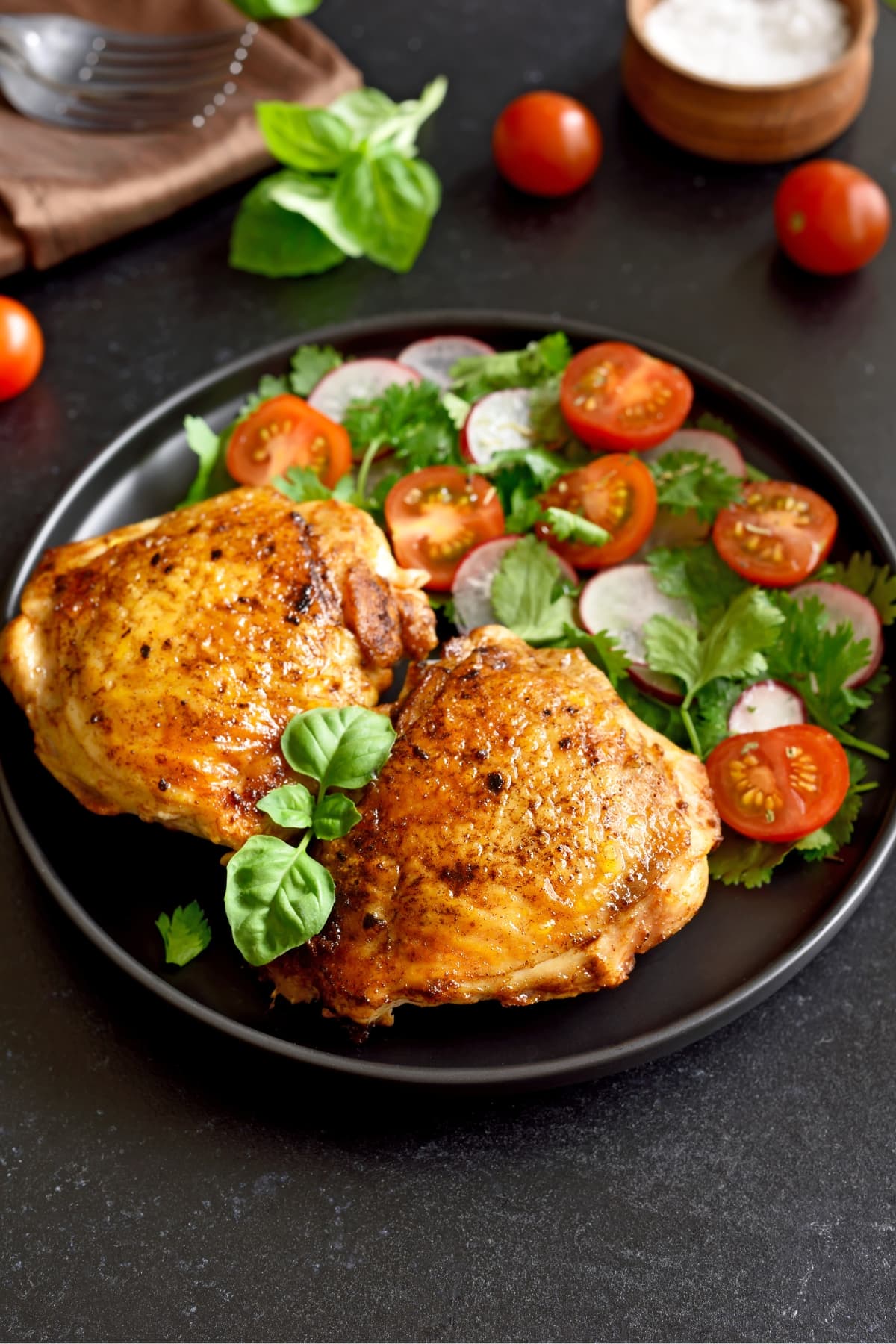Baked chicken thighs with radish, tomato, and herb salad on a plate.