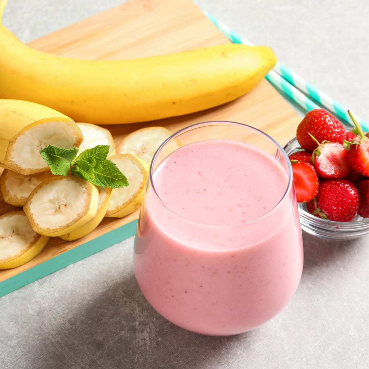 A Glass of Strawberry Smoothie with Sliced Berries and Bananas in the Background