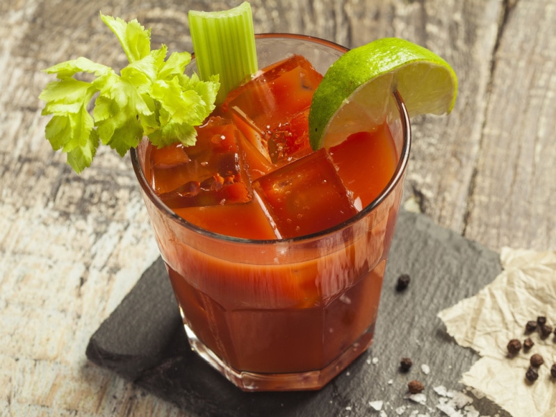 Bloody Mary Garnished with Celery and Lime Wedge over Ice On a Stone Slab with Peppercorns