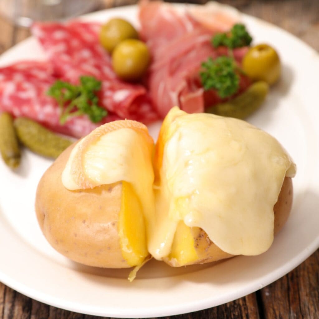 Baked Potato Poured With Raclette, Salami Slices, Pickles and Olives on Side