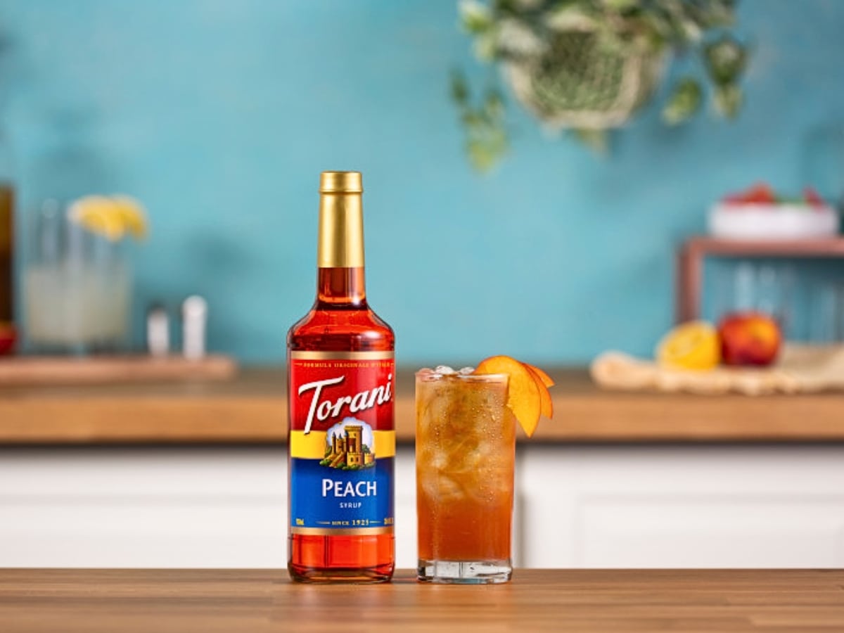 Bottle of Torani Peach Syrup and a Glass of Refreshing Peach Drink Garnished with Peach