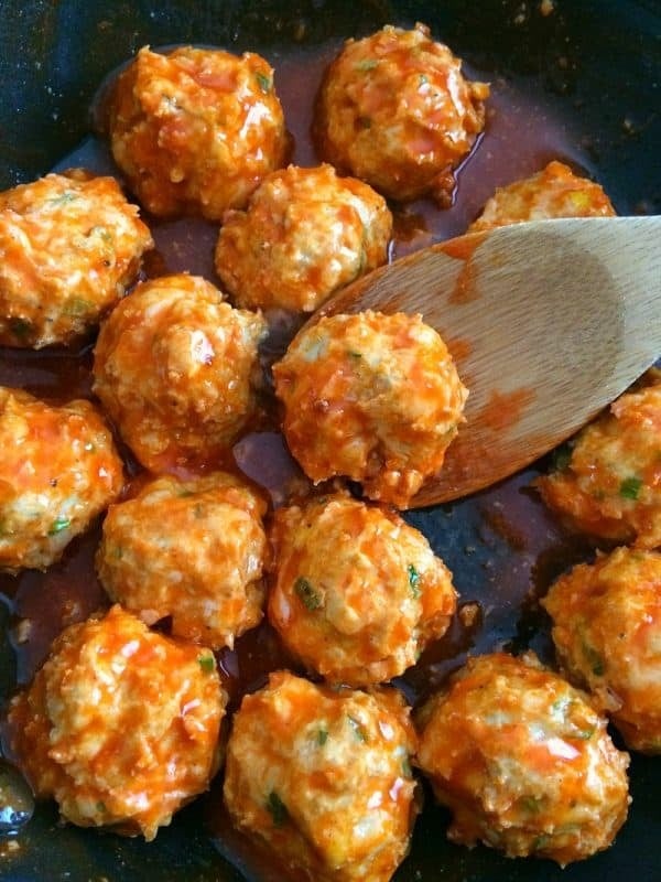 Buffalo Chicken Meatballs on a skillet with sauce tossed by a wooden ladle. 