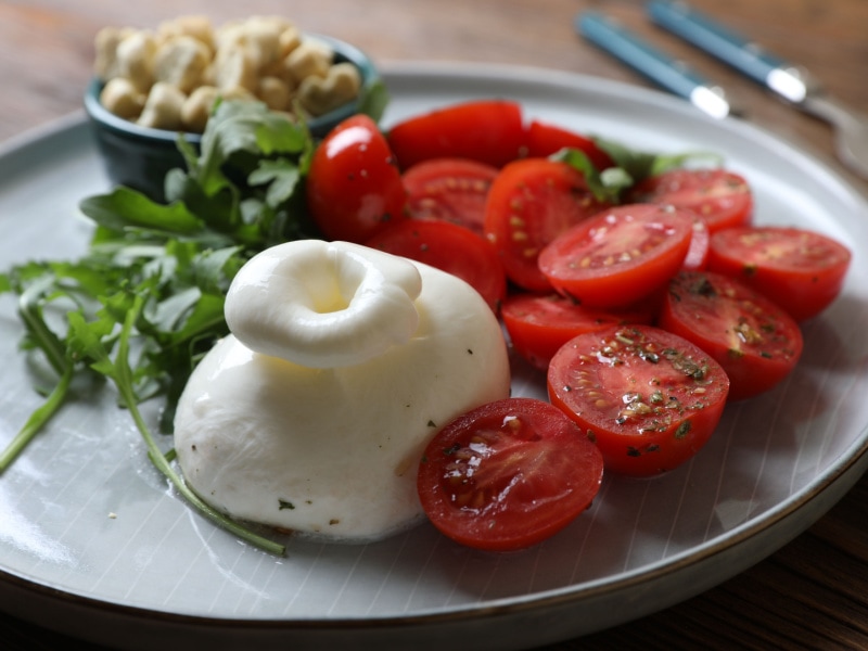 Burrata Cheese with Fresh Tomatoes Arugula and Olive Oil Serve on a Plate