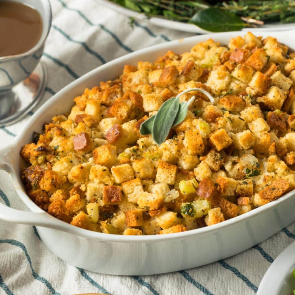 Homemade Stuffing in a Baking Dish on a Table Cloth-Covered Table with a Gravy Dish Beside It