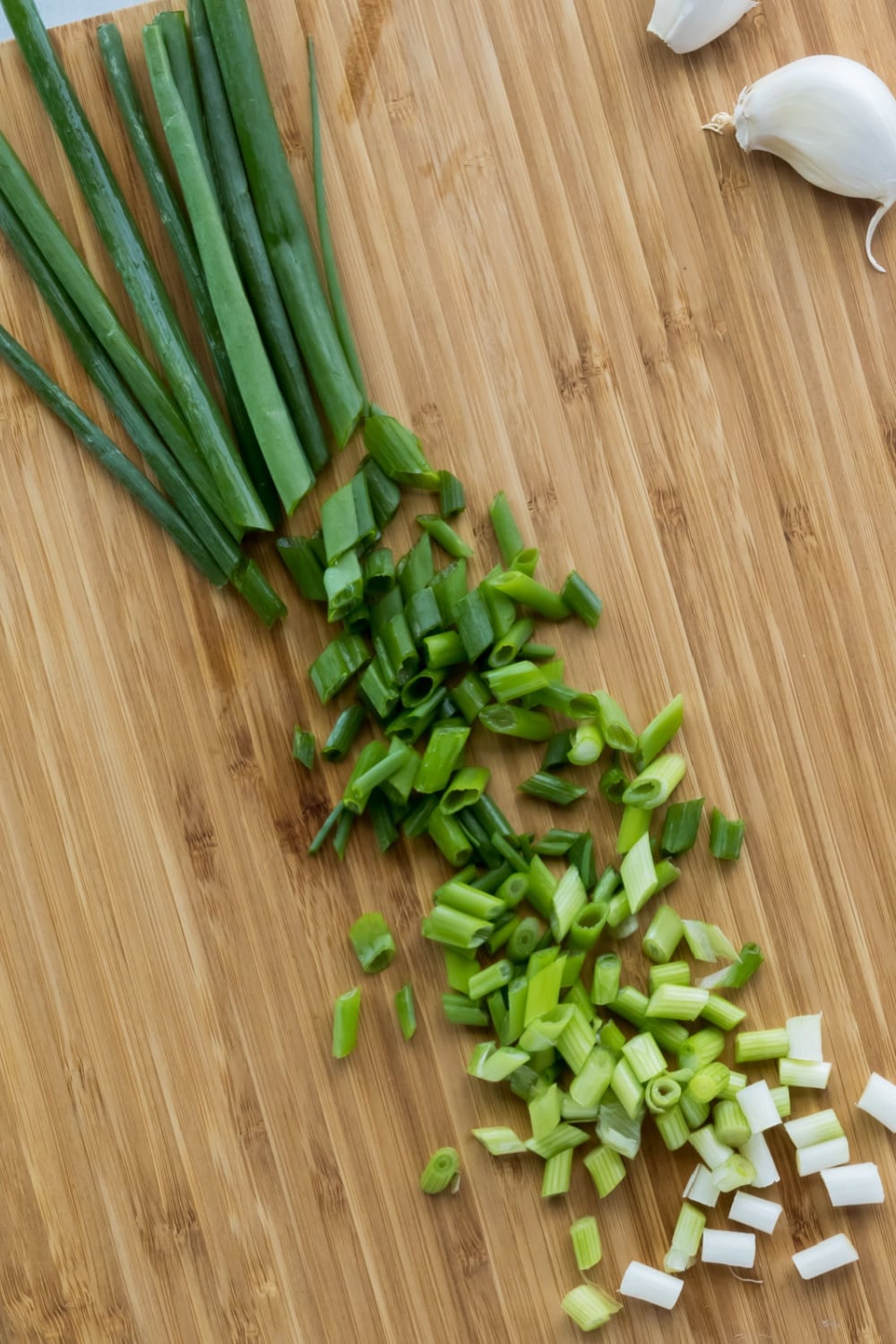 Chopped Green Onions and Cloves of Garlic on a Wooden Cutting Board