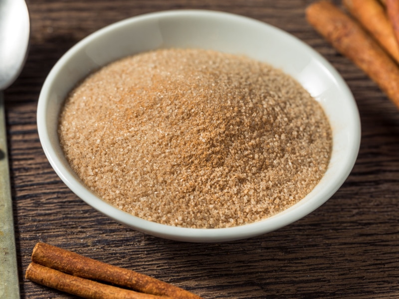  Cinnamon Sugar in a Small Bowl on a Wooden Table with Cinnamon Sticks Around the Bowl
