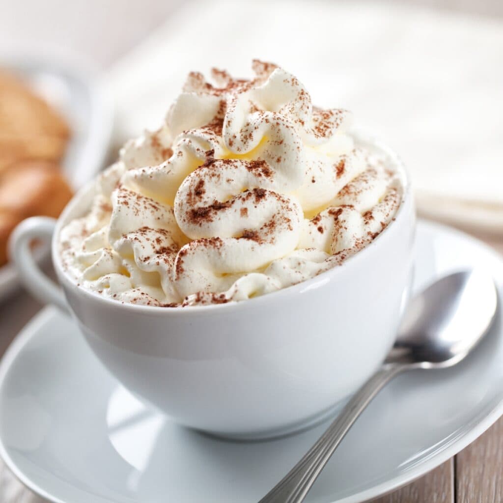 Mug of Coffee With Whipped Cream Sprinkled With Cinnamon Powder on a Saucer with a Spoon
