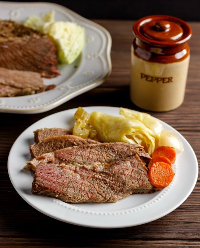 Slice of corned beef brisket served with blanched cabbage and carrots on a plate. 