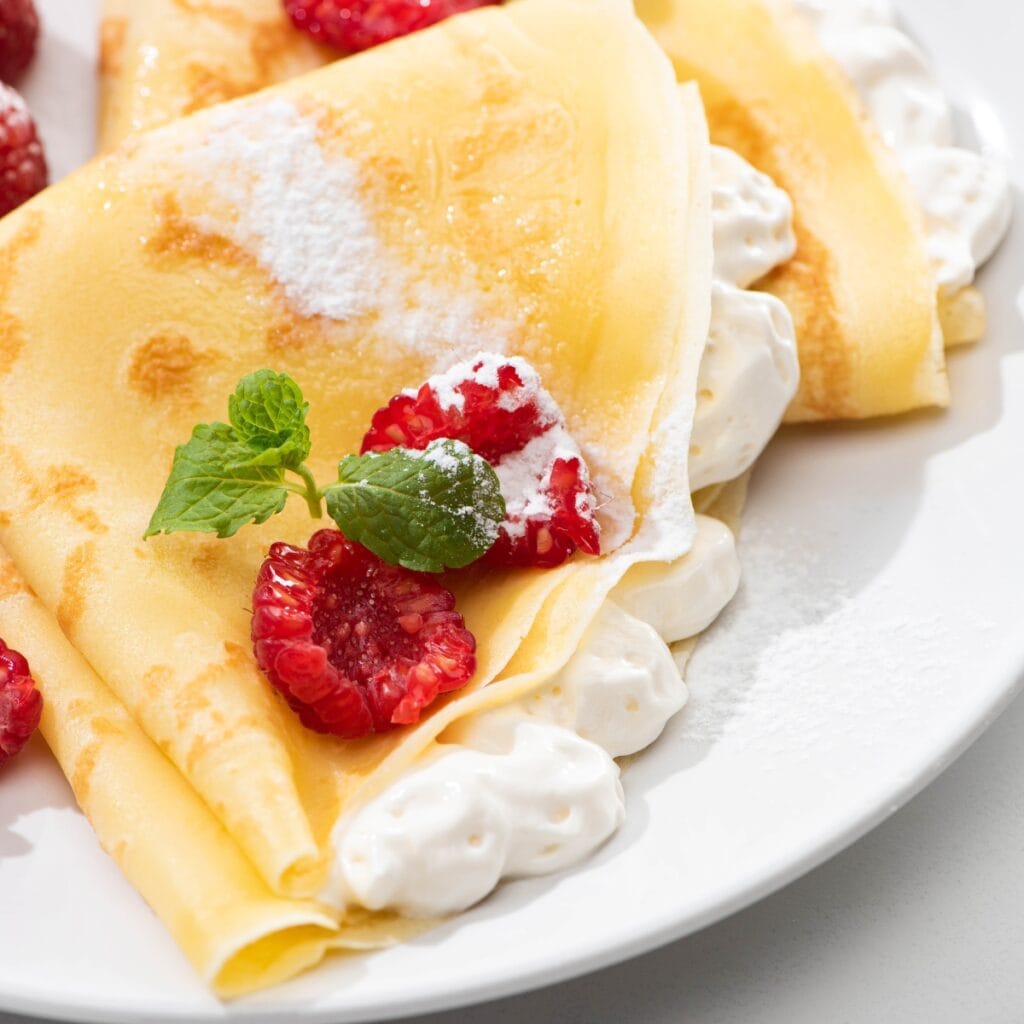 Crepes Filled With Whipped Cream Garnished With Fresh Raspberries and Sprig of Mint