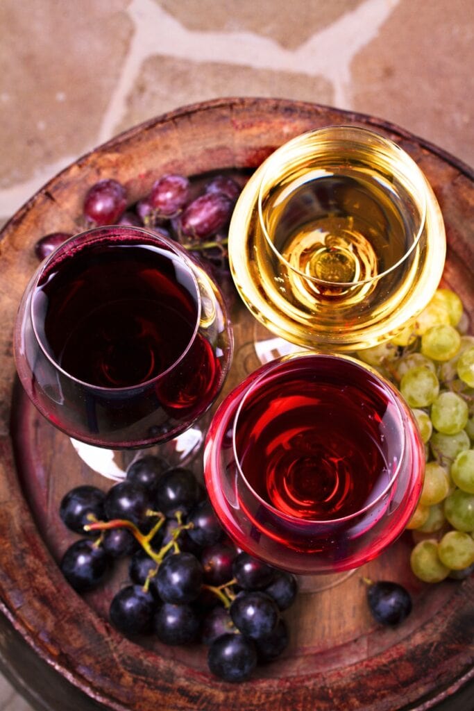 13 Popular Types of Dessert Wine To Try featuring 3 Different Dessert Wines with Fresh Grapes on a Wooden Platter
