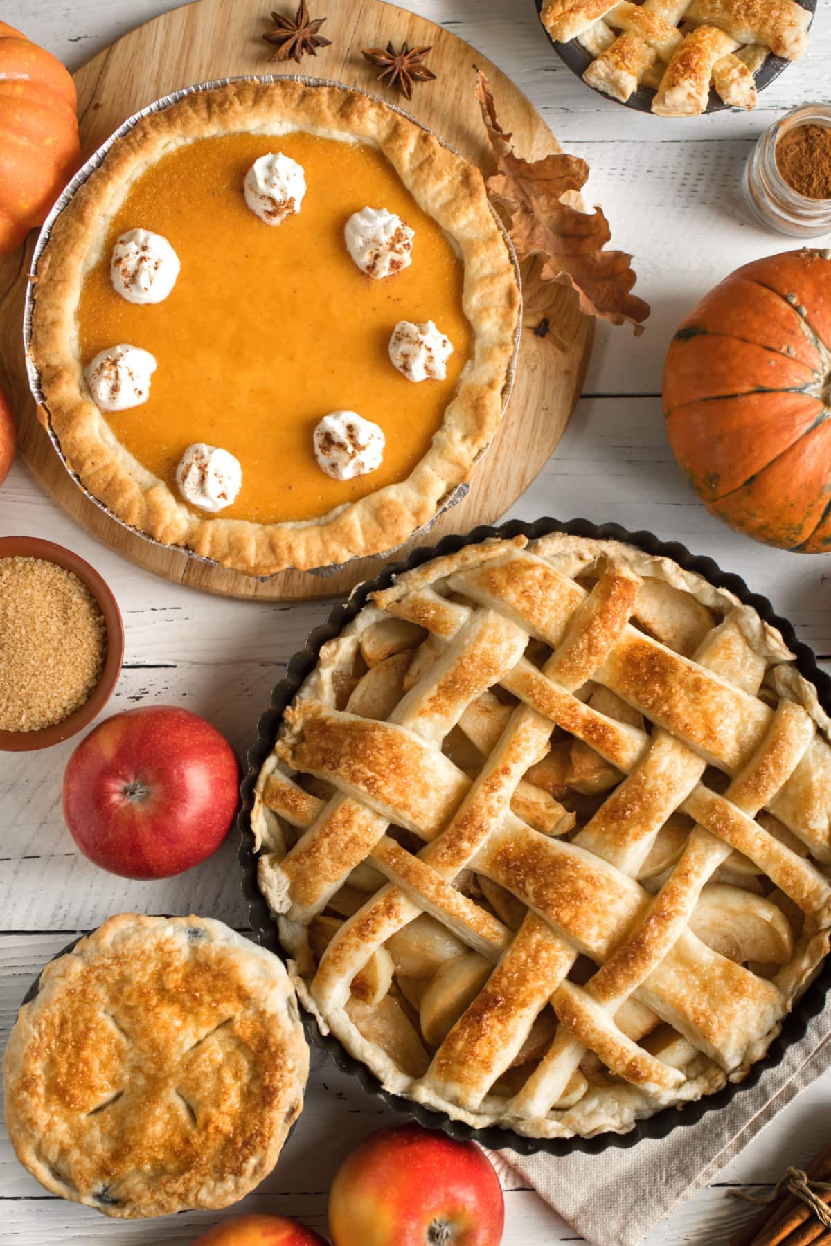 Pie vs. Tart- What's The Difference? (+ Easy Crust Recipe) featuring a Fall Table Scape with Pumpkin Pie with Whipped Cream, Lattice-Crusted Apple Pie, and a Mini Pie with Sugar, Apples, and Pumpkins Around