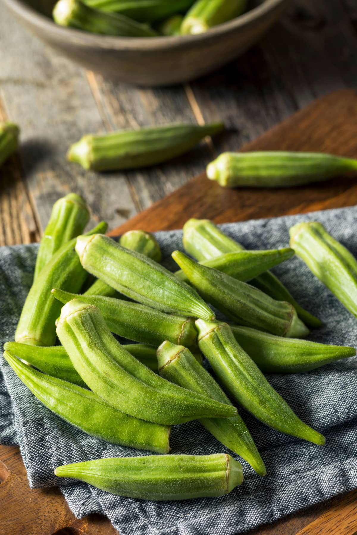 How to Freeze Okra featuring Fresh Okra on a Kitchen Towel on a Wooden Table