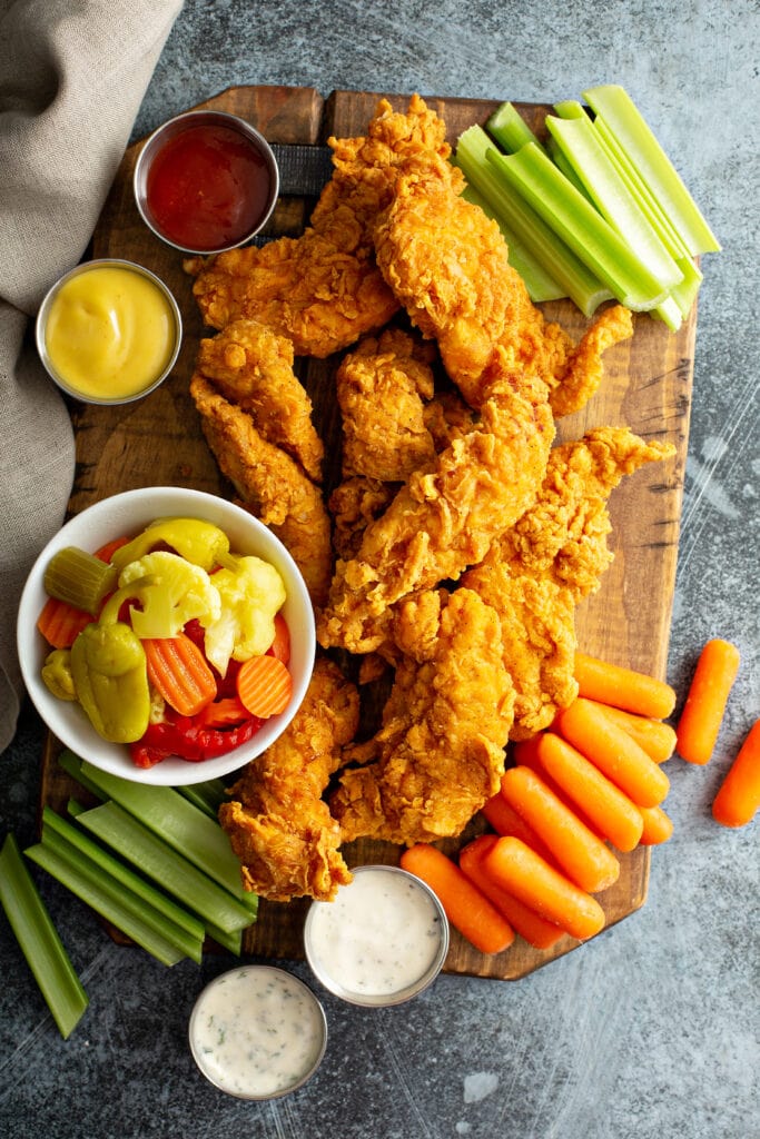 Fried Chicken Tenders with Vegetables and Dipping Sauces on a Wooden Board