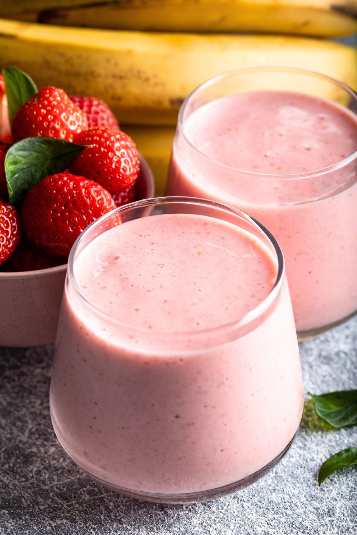 Strawberry Smoothie (Quick and Easy Recipe) featuring Two Glasses of Homemade Healthy Strawberry Smoothies and a Bowl of Fresh Strawberries