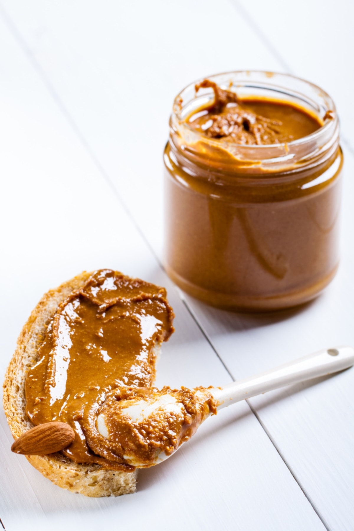 How to Make Almond Butter at Home featuring Homemade Almond Butter in a Jar and Almond Butter Spread on Slice of Bread