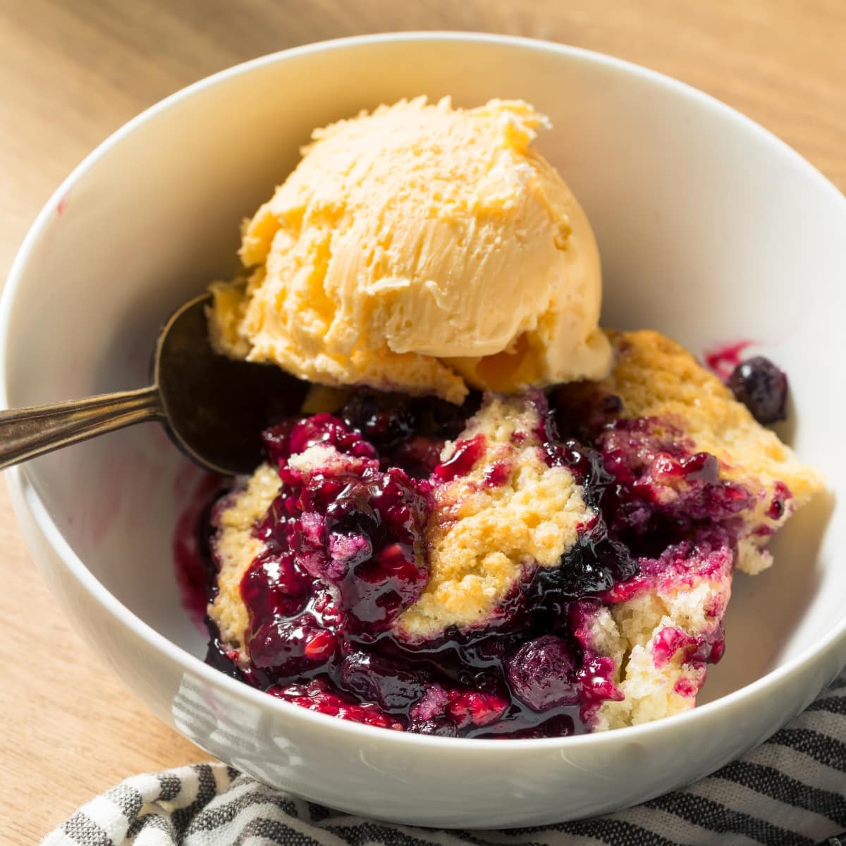 Homemade Berry Cobbler with Vanilla Ice Cream in a White Bowl with a Spoon