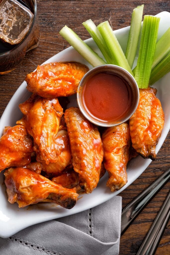 30 Best Whole30 Snacks (+ Easy Recipes) featuring Buffalo Chicken Wings with Homemade Whole30 Sauce and Celery Sticks on Wooden Table