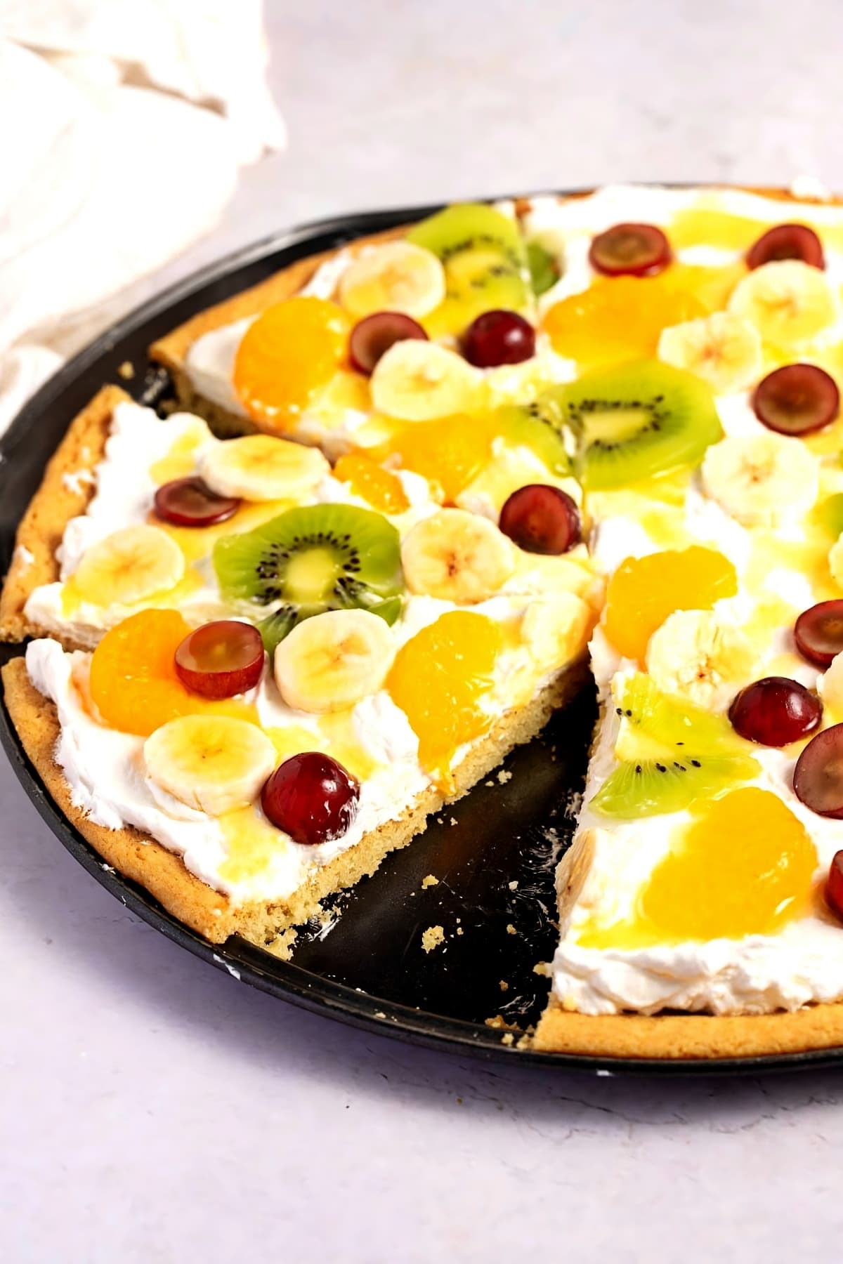 Pizza crust topped with kiwi, bananas, mandarin oranges, and grapes.