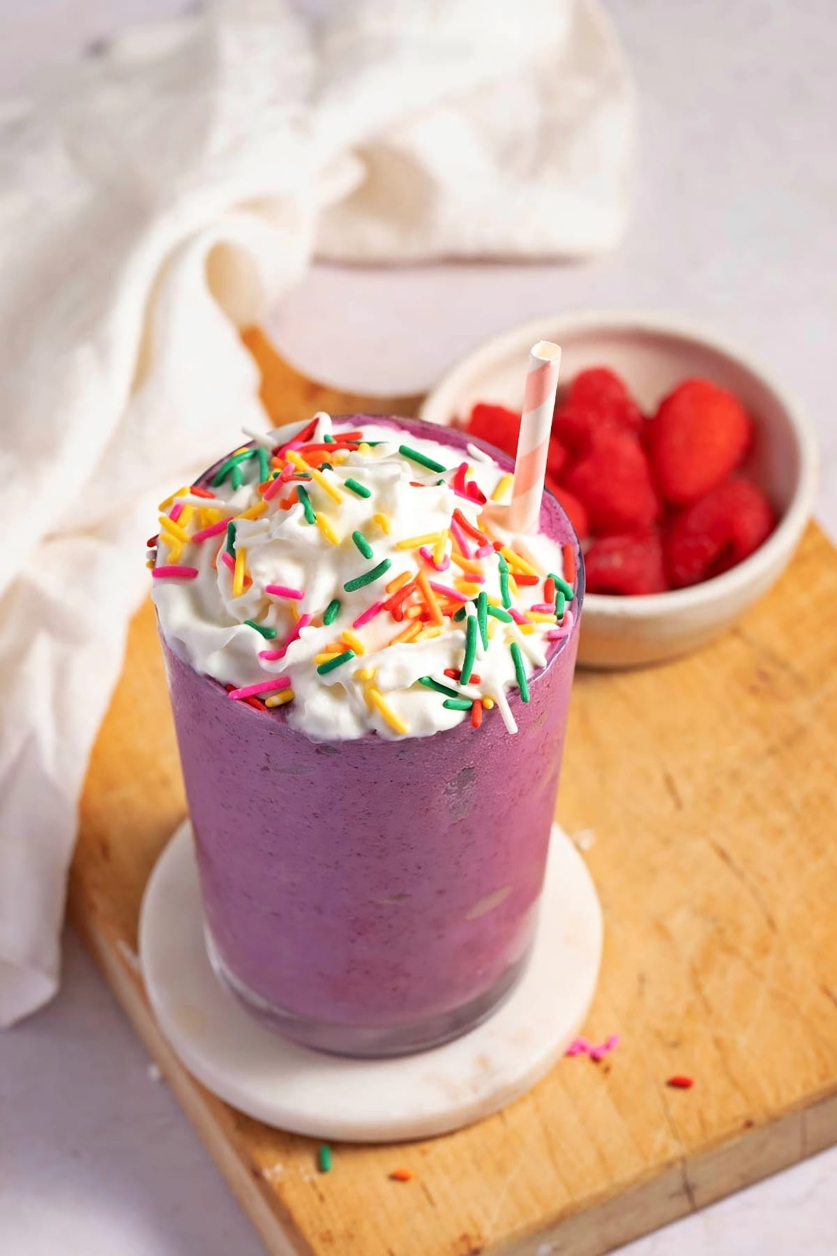 Homemade Grimace Shake with Whipped Cream, Sprinkles, and Fresh Raspberries in the Background