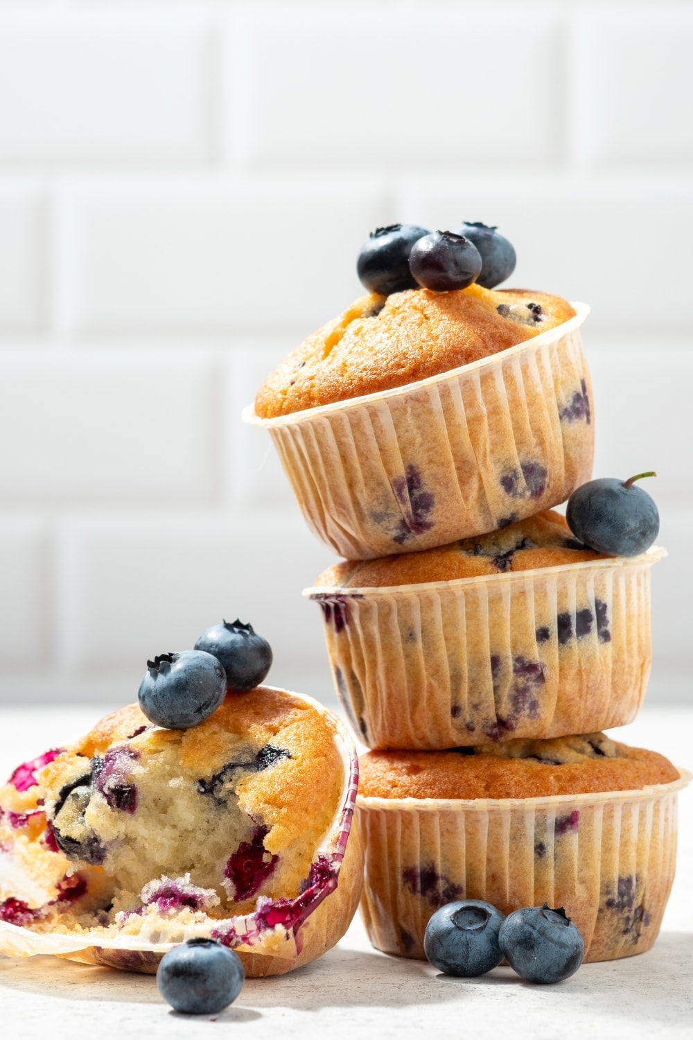 4 Fluffy Jordan Marsh Blueberry Muffins, One with a Big Bite Taken Out of It and Lots of Fresh Blueberries On and Around the Muffins