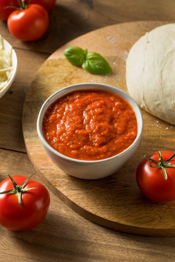 10 Best Pizza Sauce Alternatives (Easy Swaps) featuring Homemade Pizza Sauce with Fresh Tomatoes and Basil with Pizza Dough and Cheese in the Background
