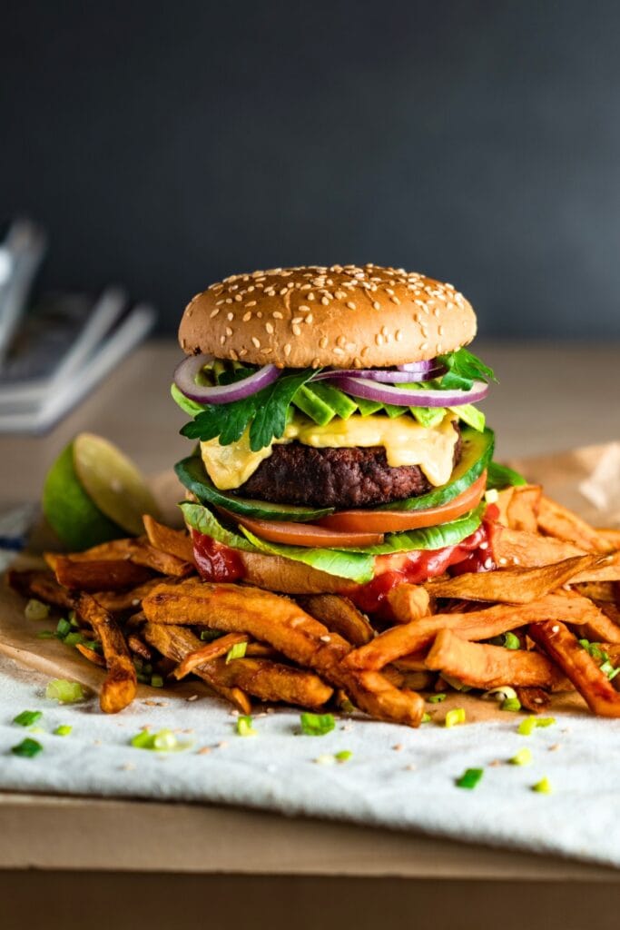 25 Easy Vegan 4th of July Recipes featuring Homemade Plant-Based Burger with Red Onion, Lettuce, Tomatoes, and Vegan Cheese with Sweet Potato Fries