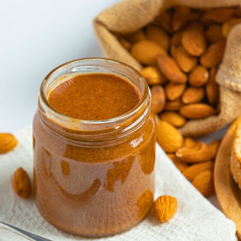 Small Jar of Homemade Almond Butter with a Sack of Almond Nuts in Background