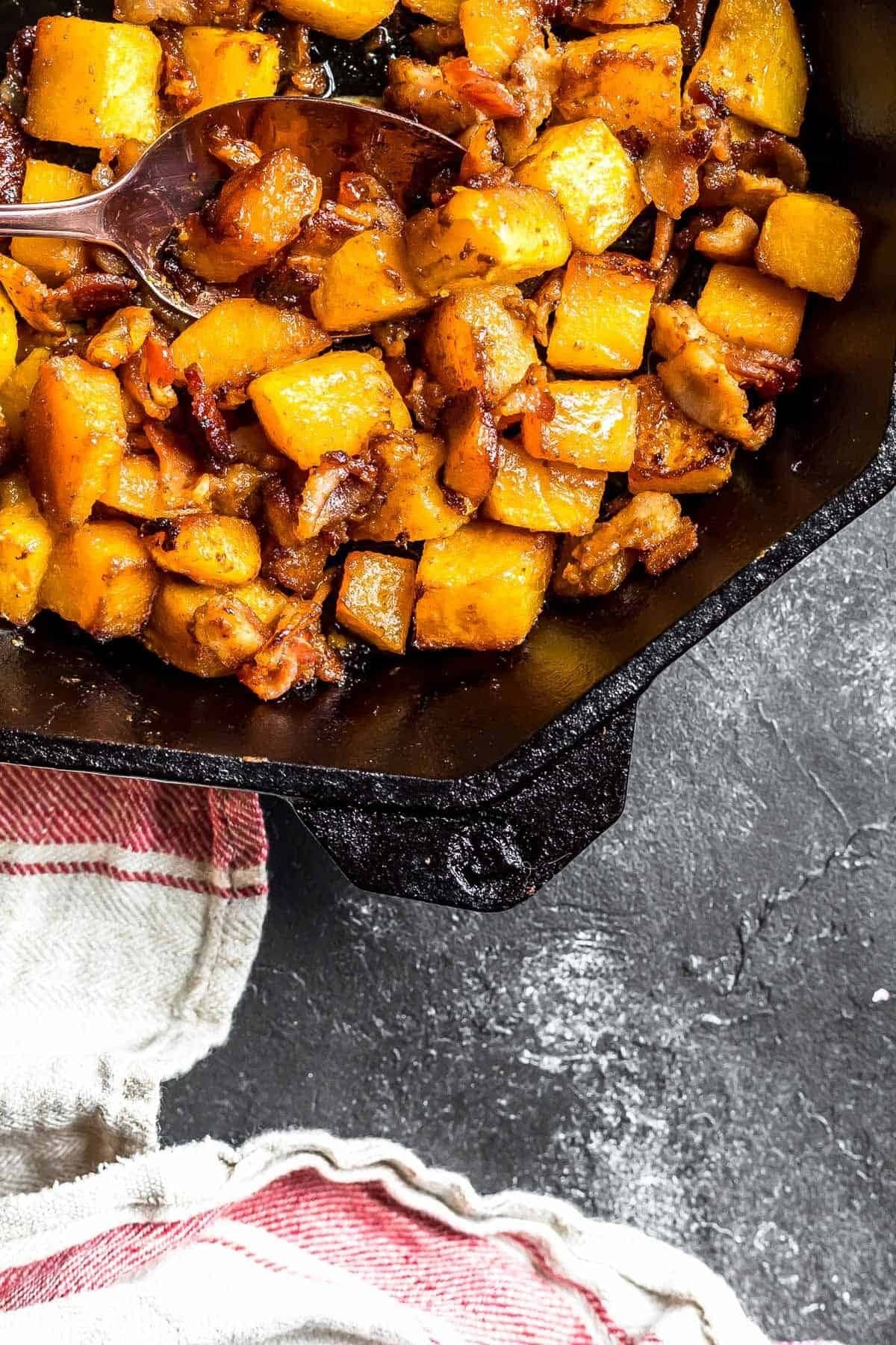 Roasted butternut squash with bacon cooked in a skillet. 