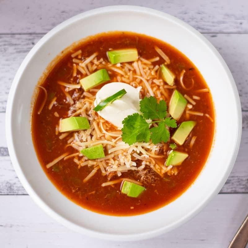 Bowl of taco soup garnished with cheese, cream and avocado. 