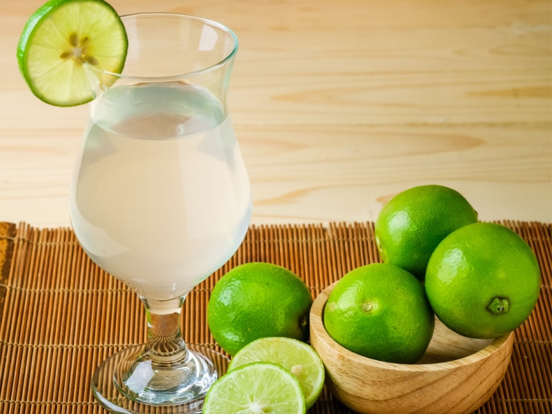 A Glass of Lime Juice and Fresh Limes in a Wooden Bowl on a Bamboo Mat