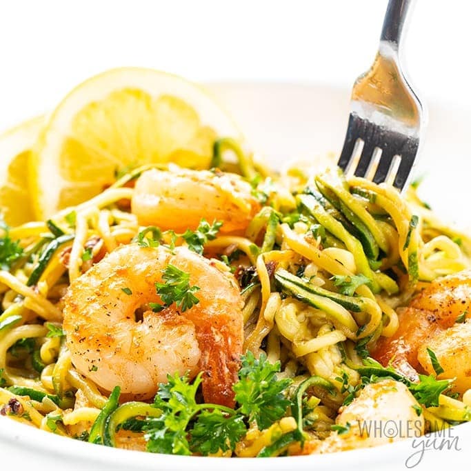 Shrimp scampi with zucchini noodles on 
white plate picked with a fork.