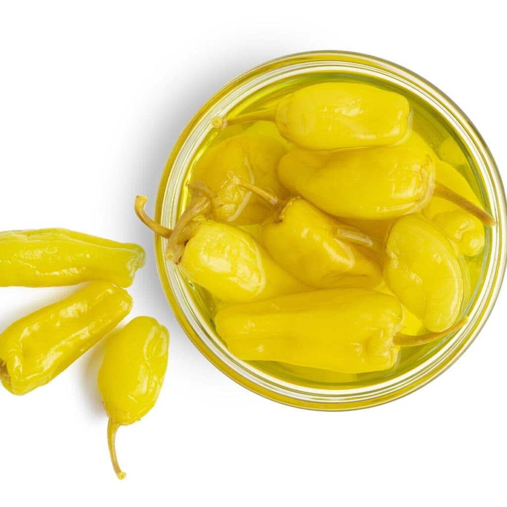 Pepperoncini Peppers Pickled in a Small Glass Jar with 3 Pepperoncini Peppers On the Side