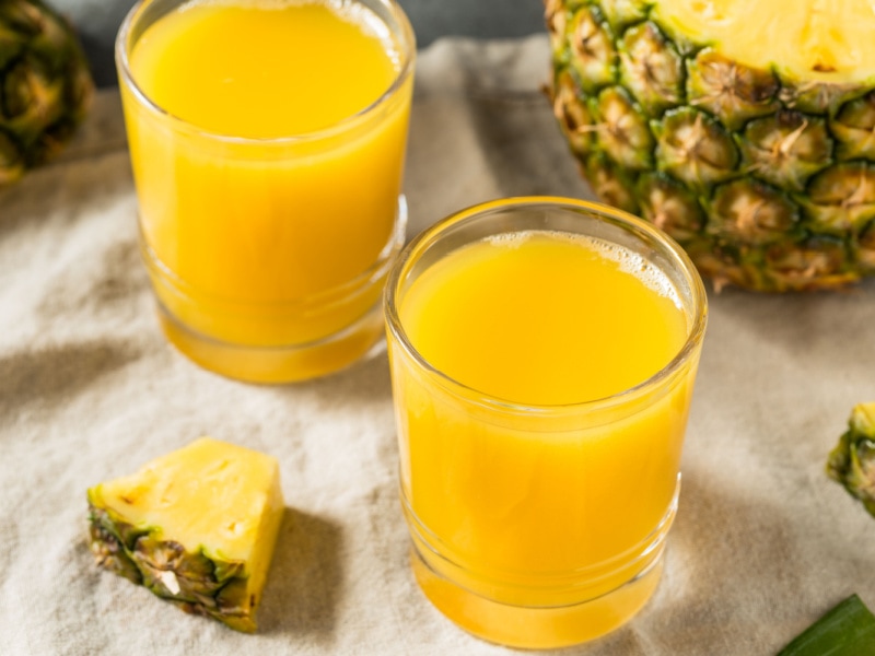 Two Glasses of Pineapple Juice and Sliced Pineapple on a Table