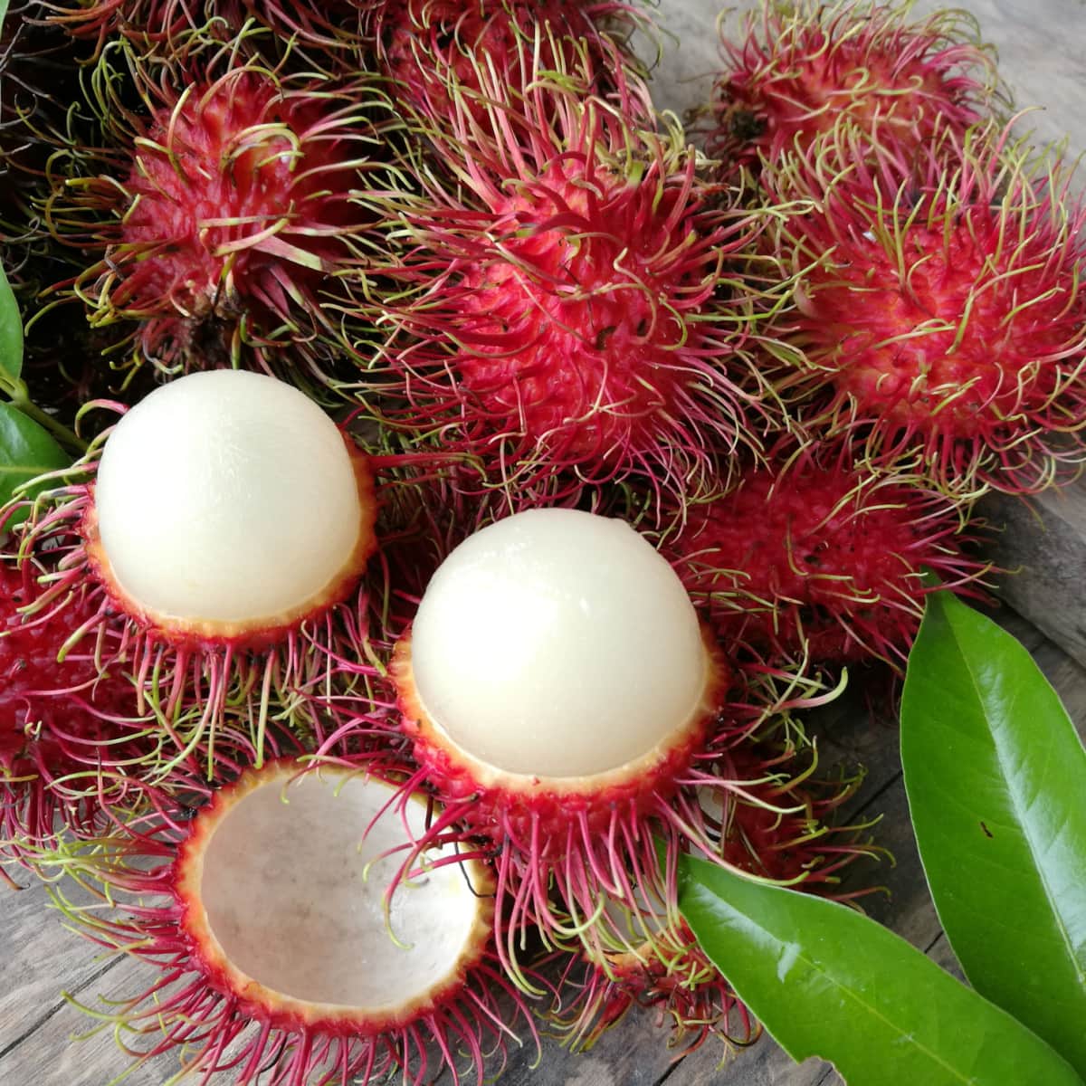 Bunch of Ripe Rambutan on a Wooden Table, Two Peeled, The Rest Unpeeled