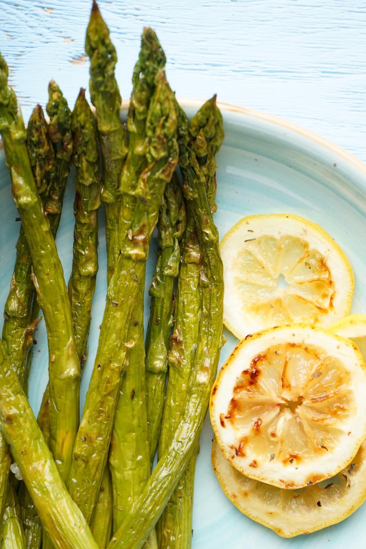 Pieces of roasted asparagus with lemon slices served on a blue plate.