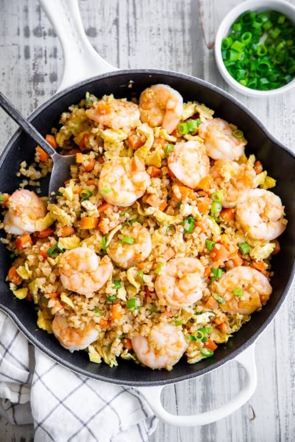Cauliflower rice cooked with shrimp and veggies on a skillet. 