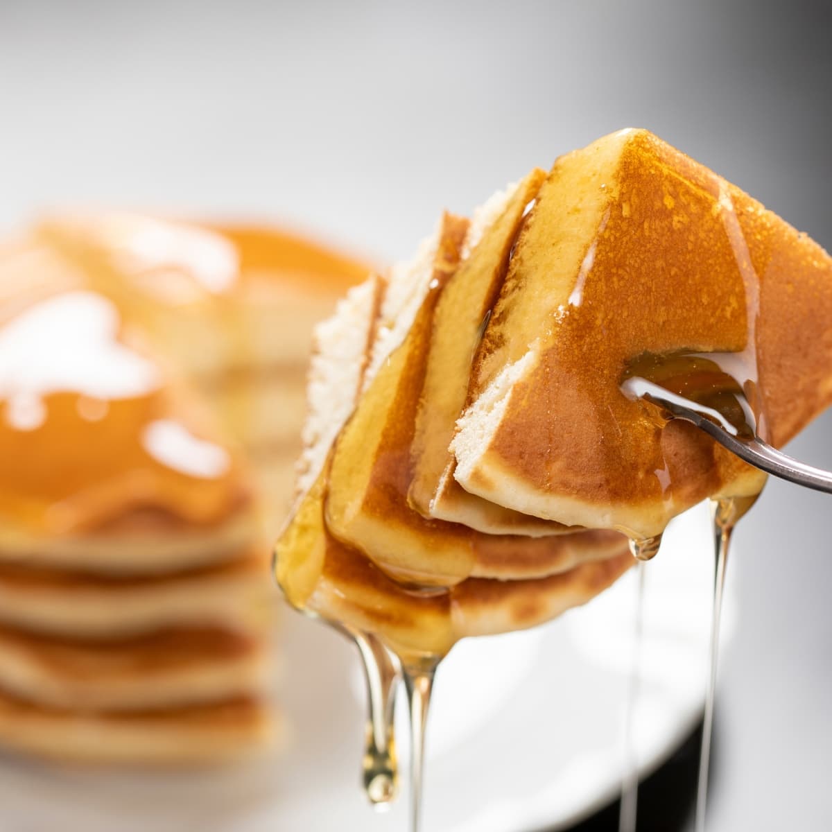 Sliced Fluffy Pancakes Picked With a Fork Dripping With Maple Syrup