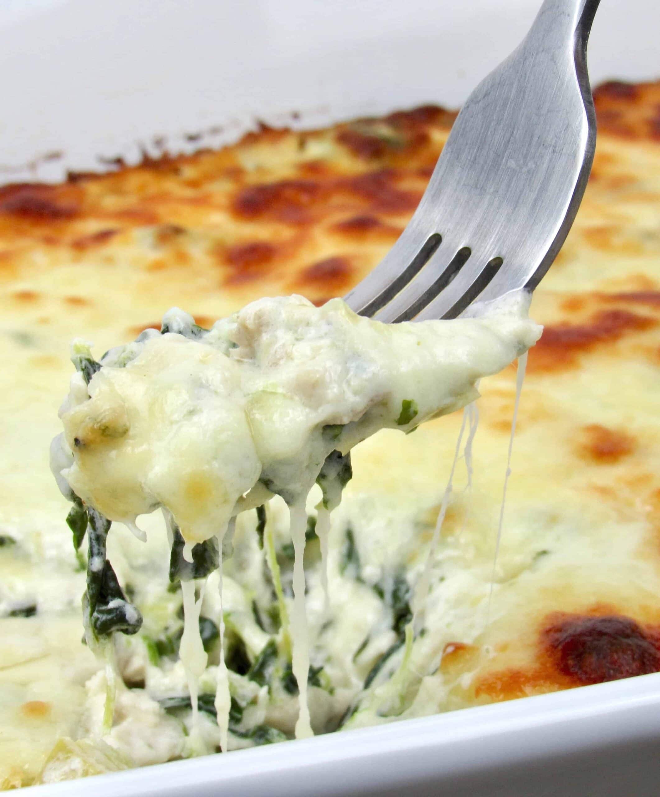 Spinach artichoke chicken in white casserole dish scooped with a fork. 