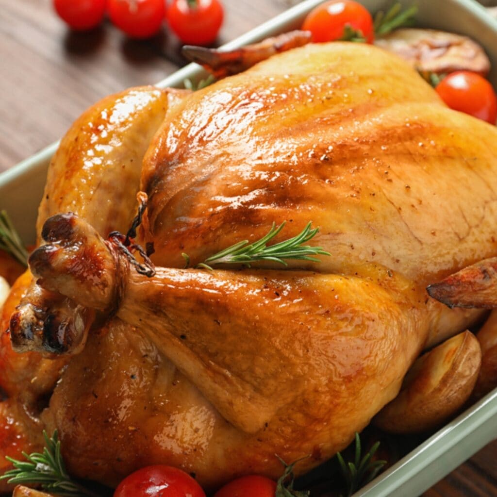 Brown and Glistening Roasted Turkey in a Roasting Pan with Potatoes, Tomatoes, and Rosemary