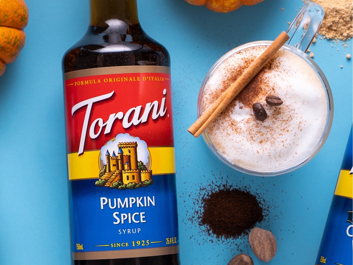 Bottle of Torani Syrup Pumpkin Spice Flavor and Pumpkin Spice Latte with Cinnamon Sticks and Coffee Beans
