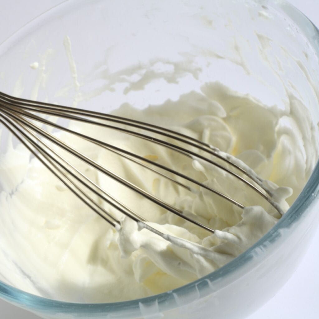 Whipping Cream Beaten By A Whisk in a Glass Bowl
