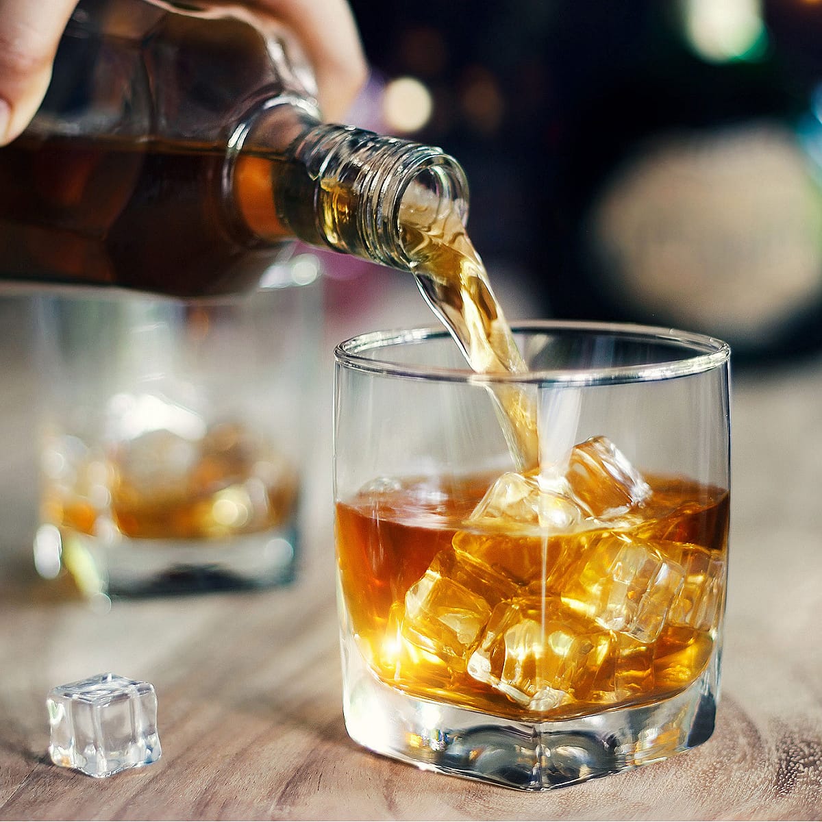 Whiskey Poured in a Glass With Ice on a Wooden Table with an Ice Cube Beside the Glass